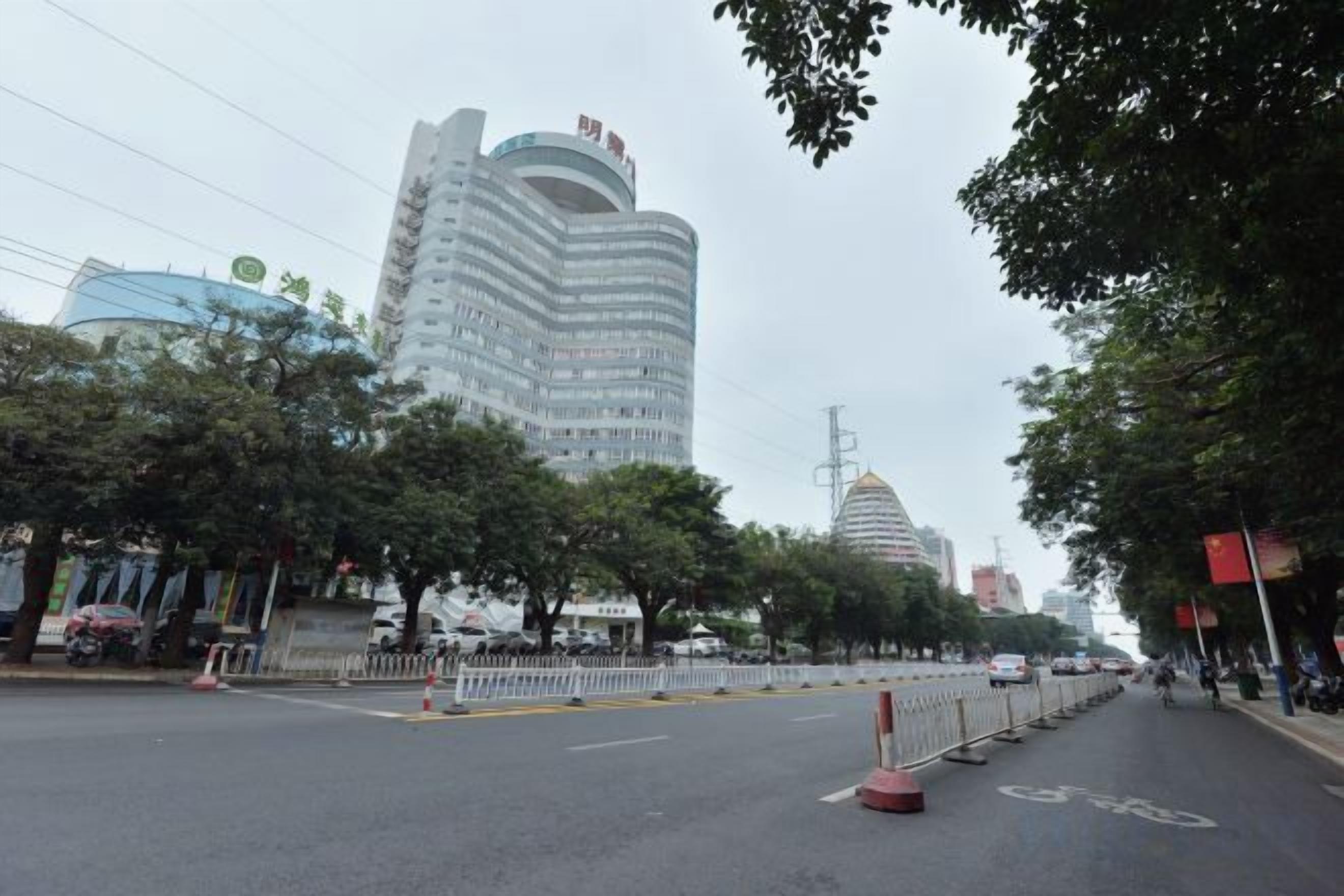 Vista de la calle con un edificio de varios pisos, árboles y una carretera despejada.