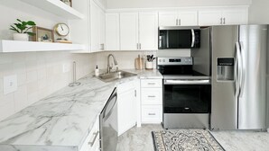 A modern kitchen with white cabinets, a stainless steel refrigerator, a microwave, and a dishwasher.