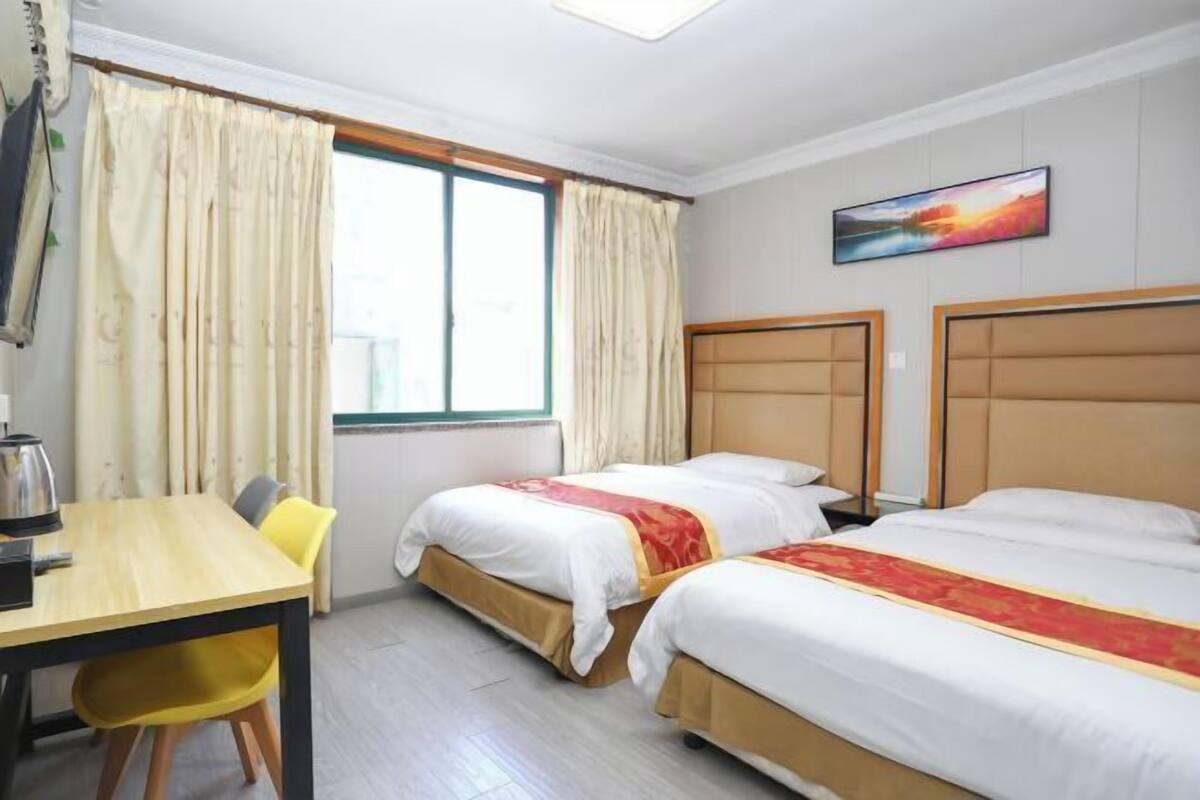 A hotel room with two beds, a wooden desk, a chair, and a window with curtains.