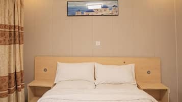 Uma cama com cabeceira de madeira, duas mesas de cabeceira, um quadro na parede e uma cortina à esquerda.