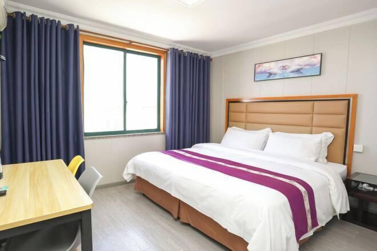 A hotel room with a bed, a desk, and a window with curtains.