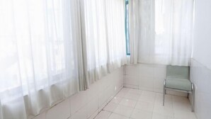 A room with a tiled floor, a green chair, and sheer curtains.