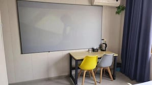 A modern room with a large flat-screen TV mounted on the wall, a wooden table with two chairs, and an air conditioning unit above the table.