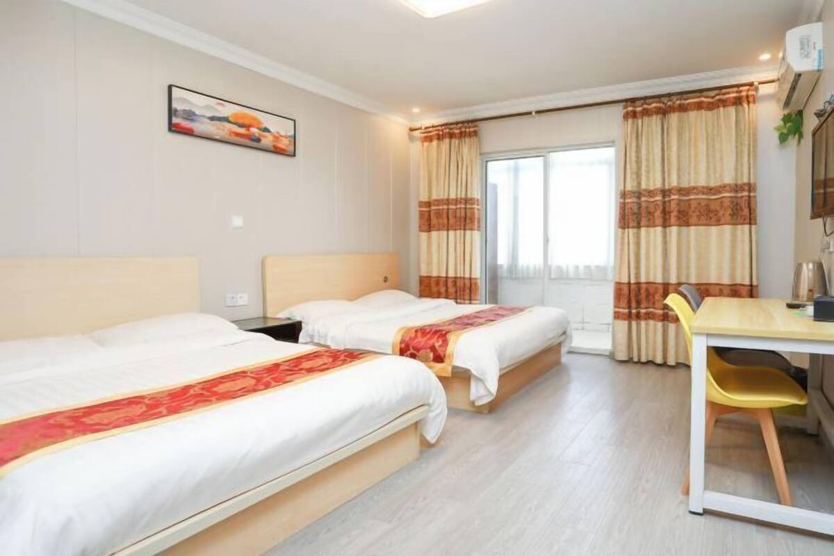 A hotel room with two single beds, a desk, a chair, and a large window with curtains.