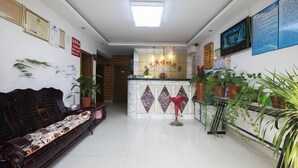 A hotel lobby with a reception desk, a sofa, and potted plants.