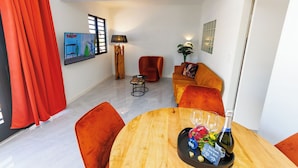 A modern living room with a wooden dining table, red curtains, a sofa, and a TV on the wall. - Las Palmeras Apartments (Willemstad)