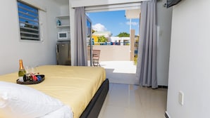 A hotel room with a bed, a minibar, a microwave, and a view of the outside balcony. - Las Palmeras Apartments (Willemstad)