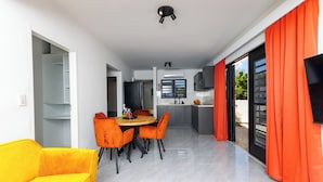 A modern kitchen with grey cabinets, a black refrigerator, and a window with orange curtains. - Las Palmeras Apartments (Willemstad)