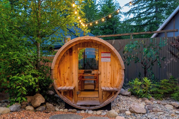 A wooden sauna structure with benches inside, surrounded by rocks and greenery.