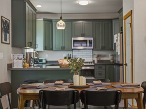 A dining area with a wooden table, black chairs, and a vase with greenery.