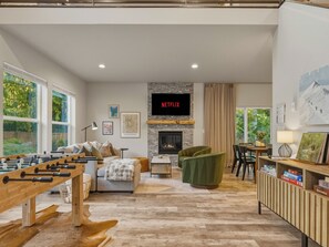 A modern living room with a foosball table, a fireplace, a television, and a dining area.
