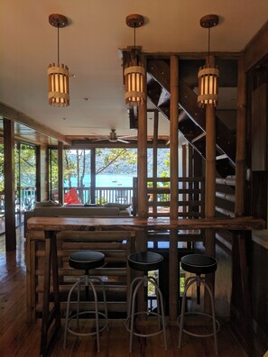 Un coin bar en bois avec des tabourets, un escalier et une vue sur un lac.