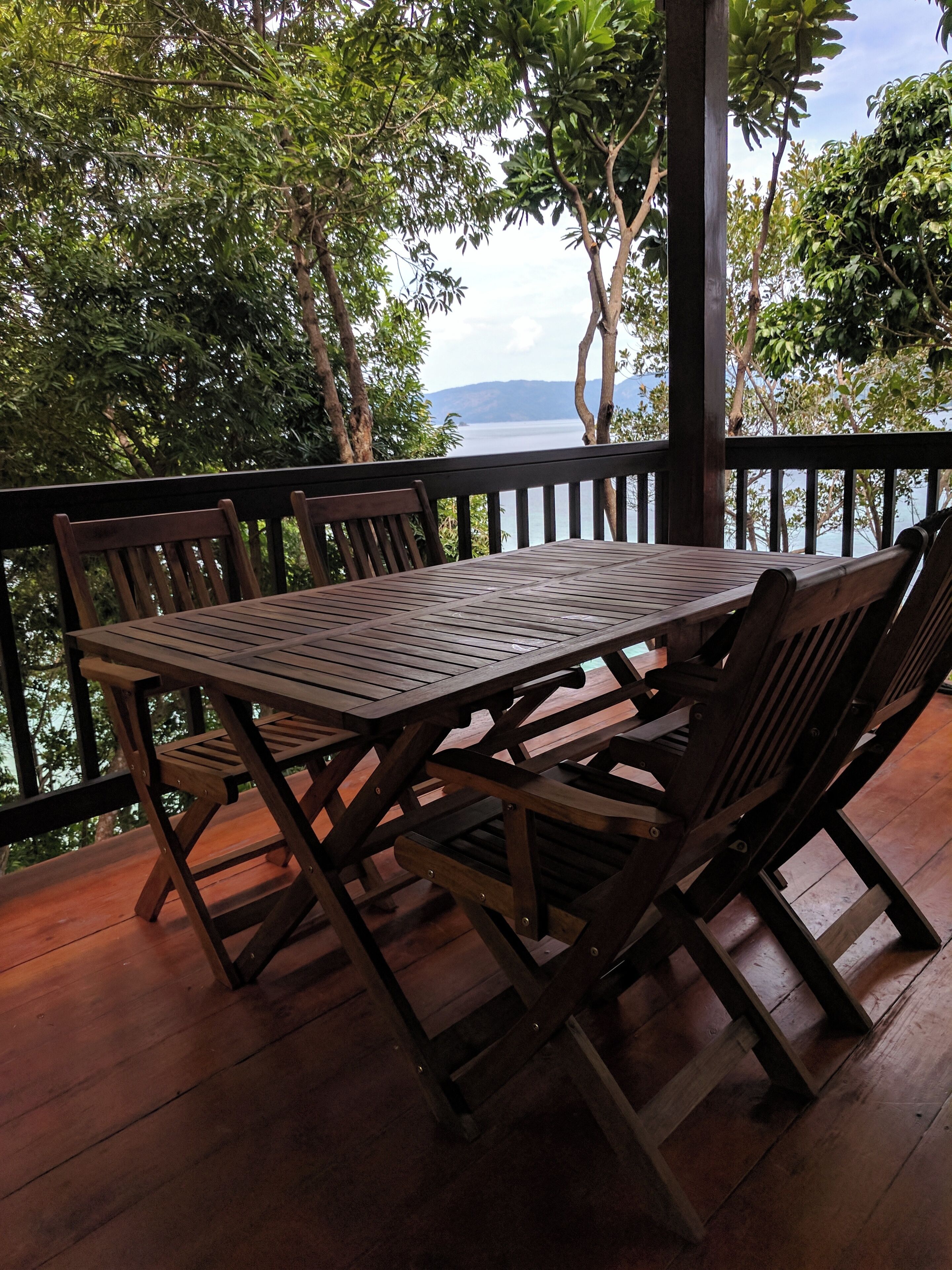Una terraza de madera con una mesa y sillas, con vista a una masa de agua y vegetación.