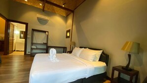 A hotel room with a large bed, wooden flooring, a nightstand with a lamp, a wardrobe, and an air conditioning unit. - Cashewnut Cove Bungalow - Beach Front (Ko Lipe)
