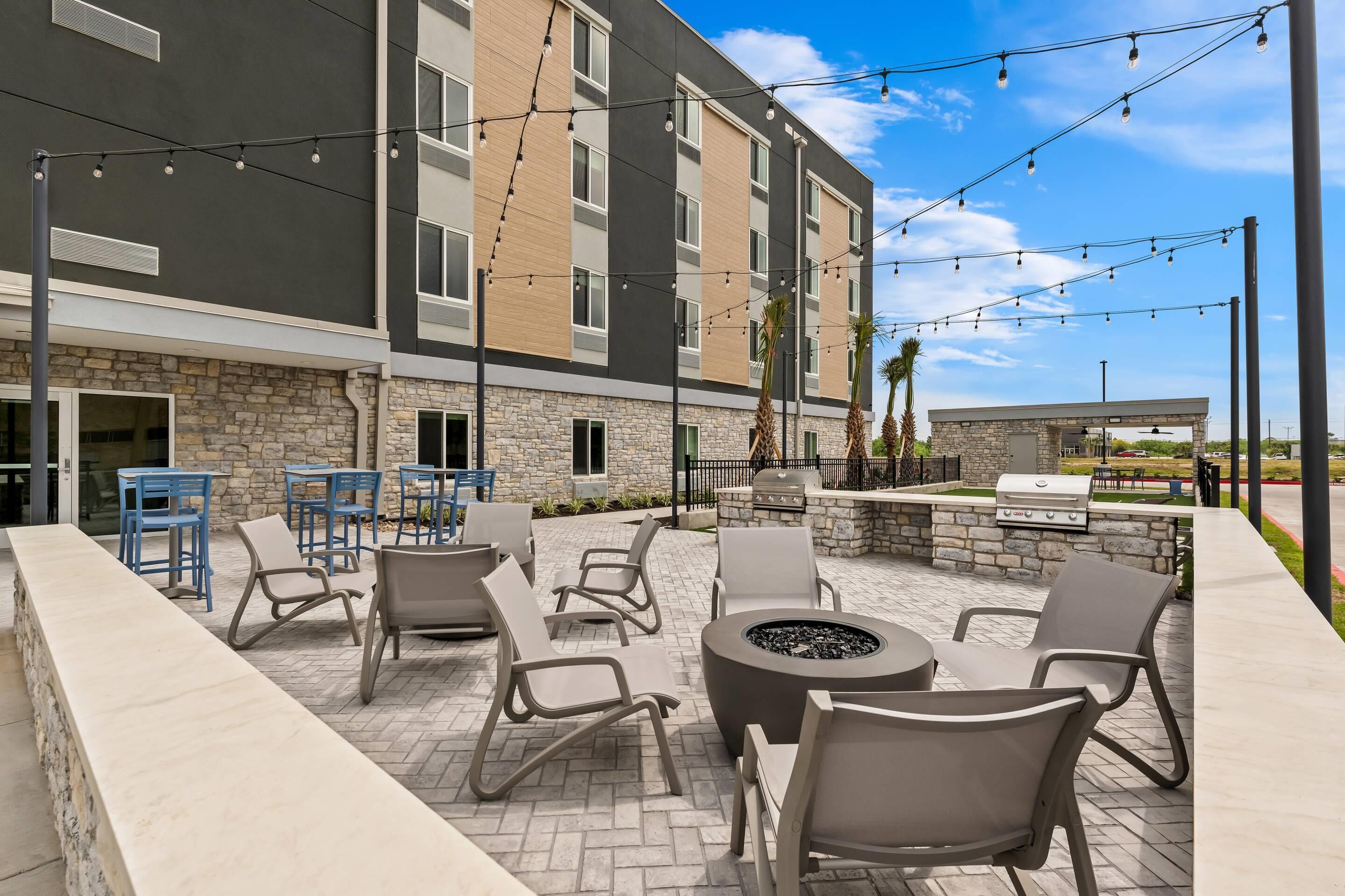 An outdoor patio with seating and a fire pit, stone walls, and string lights.