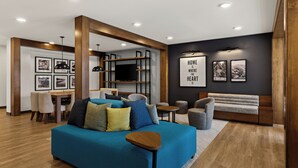 Una sala de estar moderna con un sofá azul, vigas de madera, una zona de comedor y cuadros en las paredes.