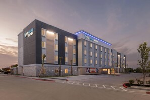 Un hotel con diseño moderno, que destaca un letrero grande de 'EverHome Suites' y un mural llamativo en la fachada.