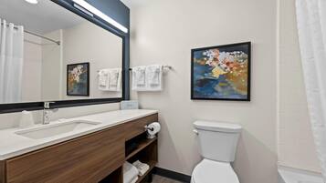 A modern bathroom with a wooden vanity, white sink, and a large mirror. There is a toilet and a shower area with a white curtain.