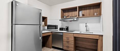 Una cocina moderna con un refrigerador de acero inoxidable, un microondas, una cafetera y armarios de madera.