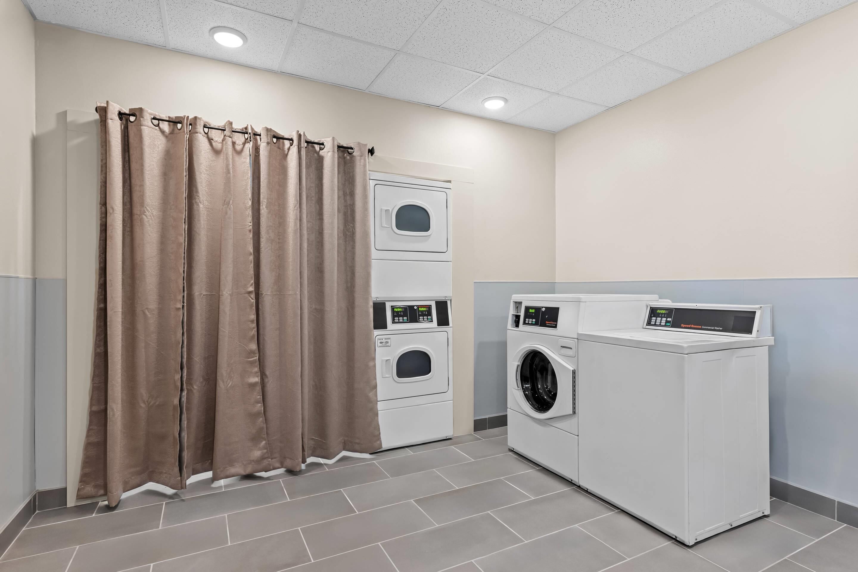Une buanderie avec un rideau marron, une machine à laver et un sèche-linge superposés, et un lave-linge à chargement frontal.
