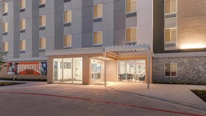 Una entrada de hotel moderna con fachada de vidrio, pared de piedra y un mural de un futbolista.