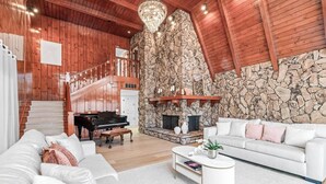 A spacious living room with a grand piano, a white sofa, and a stone wall. - 13-Acre Luxury Estate, Pool, Jacuzzi, Basket/Pickleball, Mini-golf, Sleeps 20+ (Modesto)
