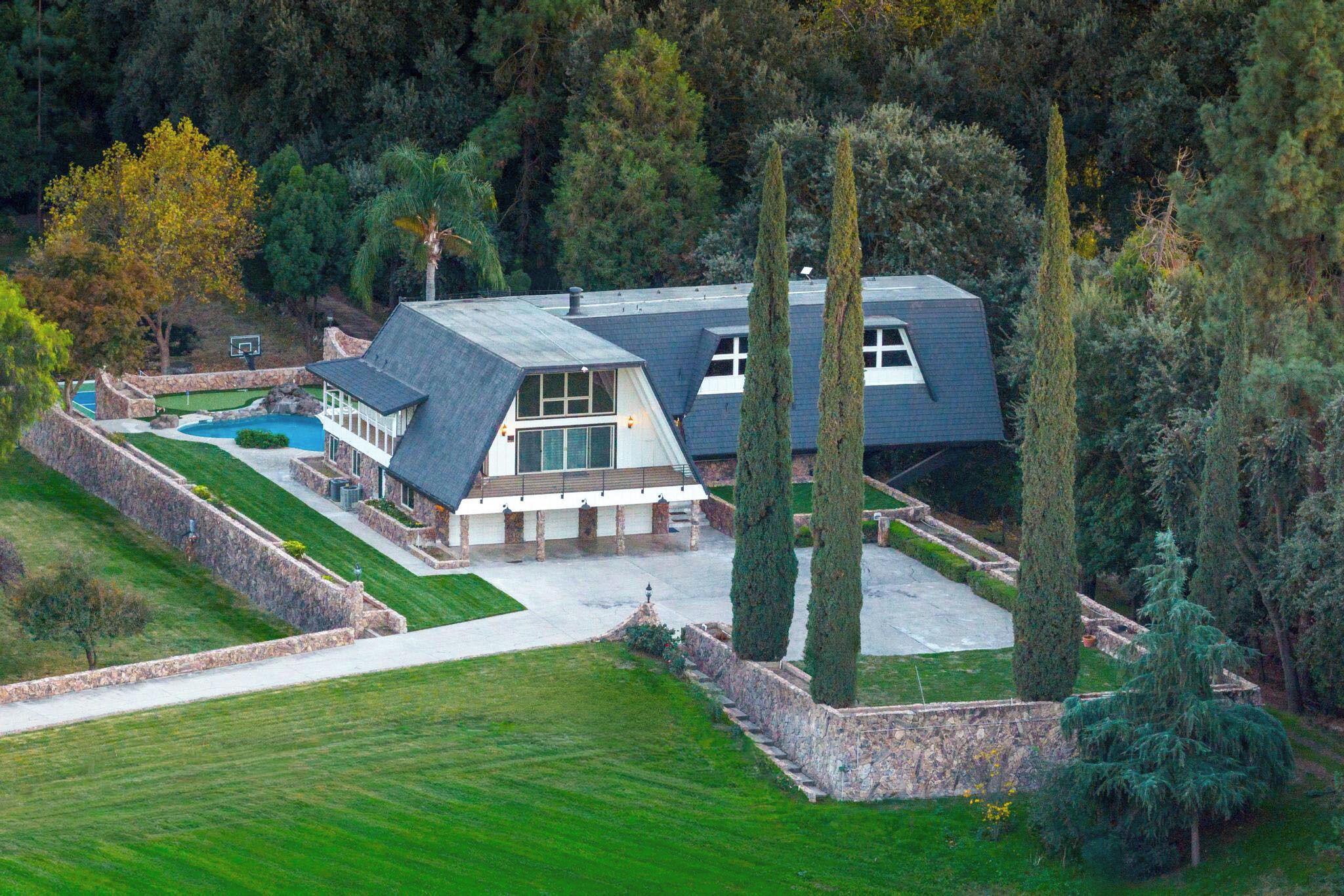 Un'ampia casa moderna con piscina, circondata da un prato curato e alberi alti.
