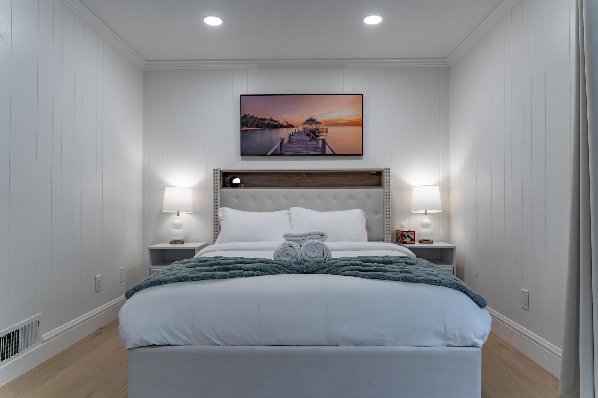 Quarto com uma cama grande, duas mesas de cabeceira com abajures, um quadro na parede e um painel de cabeceira de madeira.