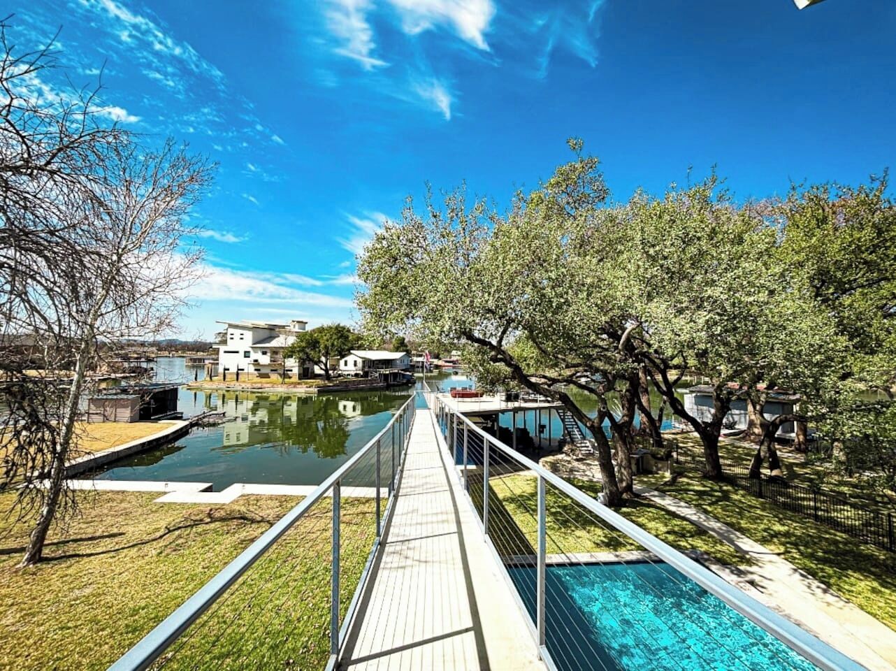 A wooden deck leading to a swimming pool with a clear view of a lake and buildings in the background.
