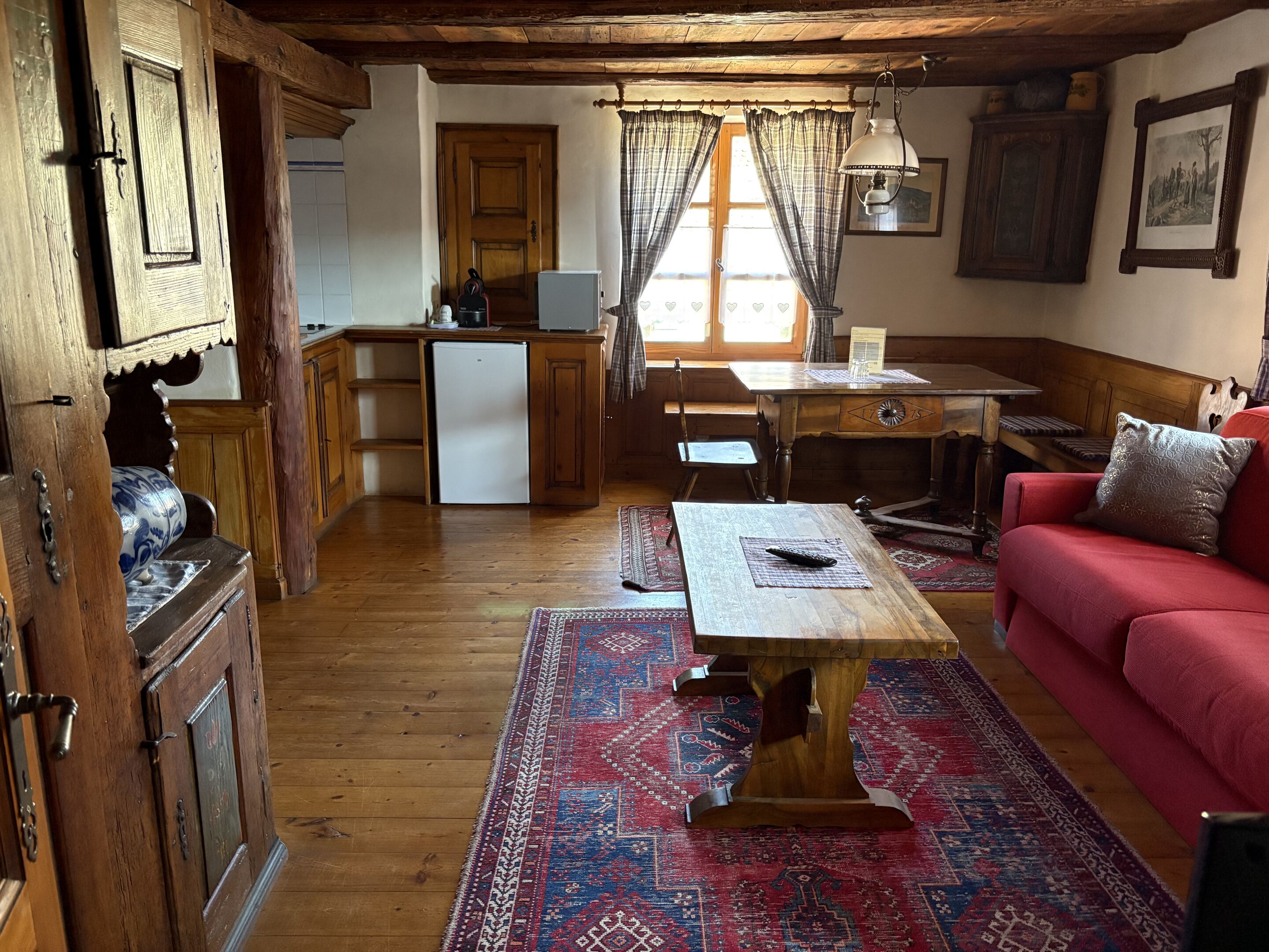 Een klassieke kamer met houten meubels, een rode bank, een houten tafel en een vloerkleed met dessin.