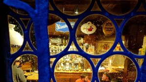 Egy bár, melynek több kör alakú ablaka van, egy „Kunstler” feliratú tábla és egy „Pilsner” sörreklám látható rajta.