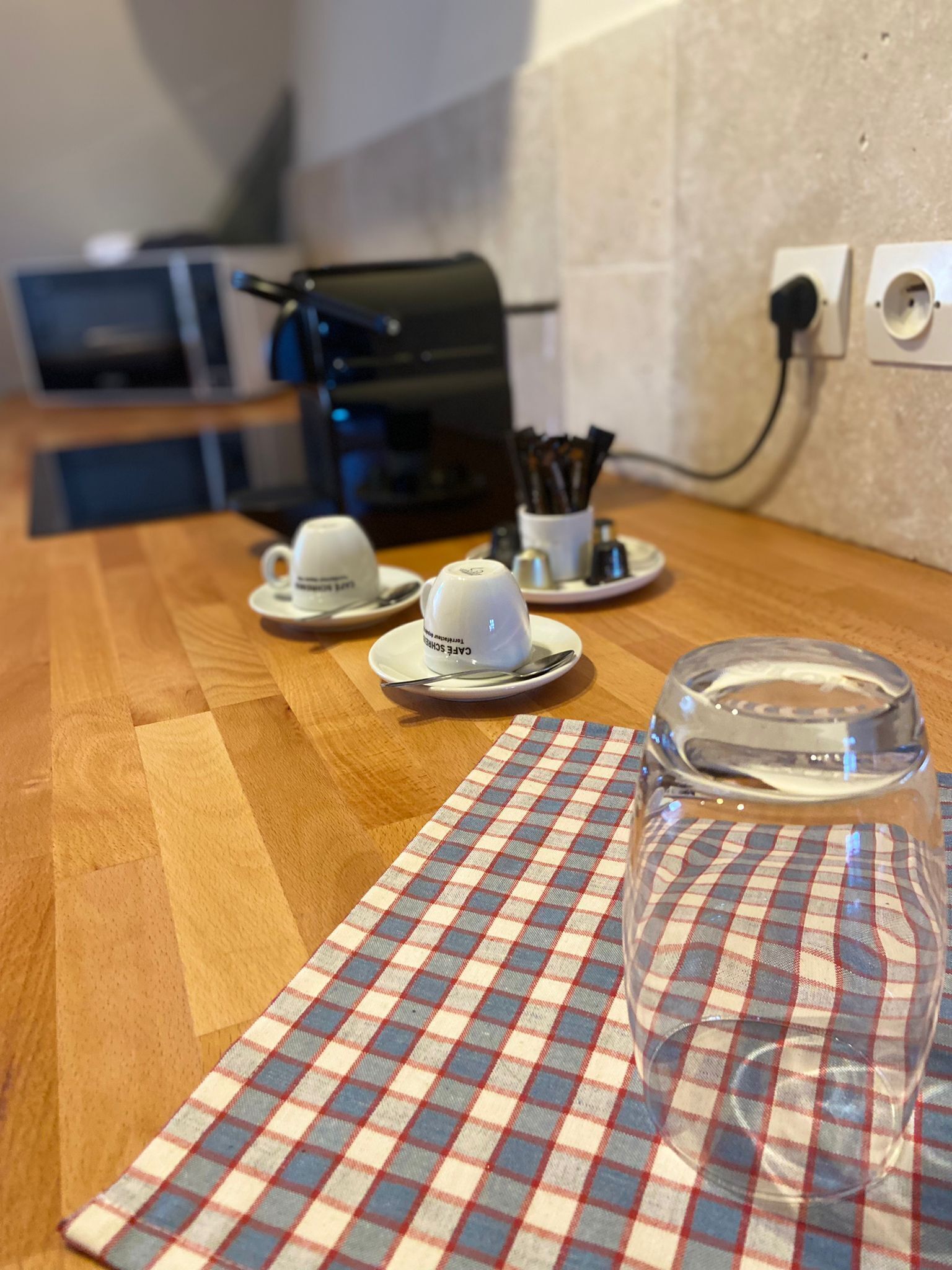 A kitchen counter with a checkered placemat, two white coffee cups, and a clear glass.
