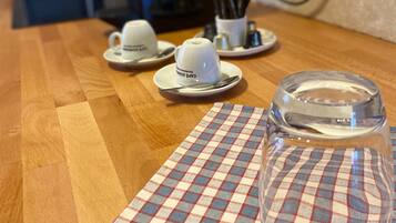 A kitchen counter with a checkered placemat, two white coffee cups, and a clear glass.