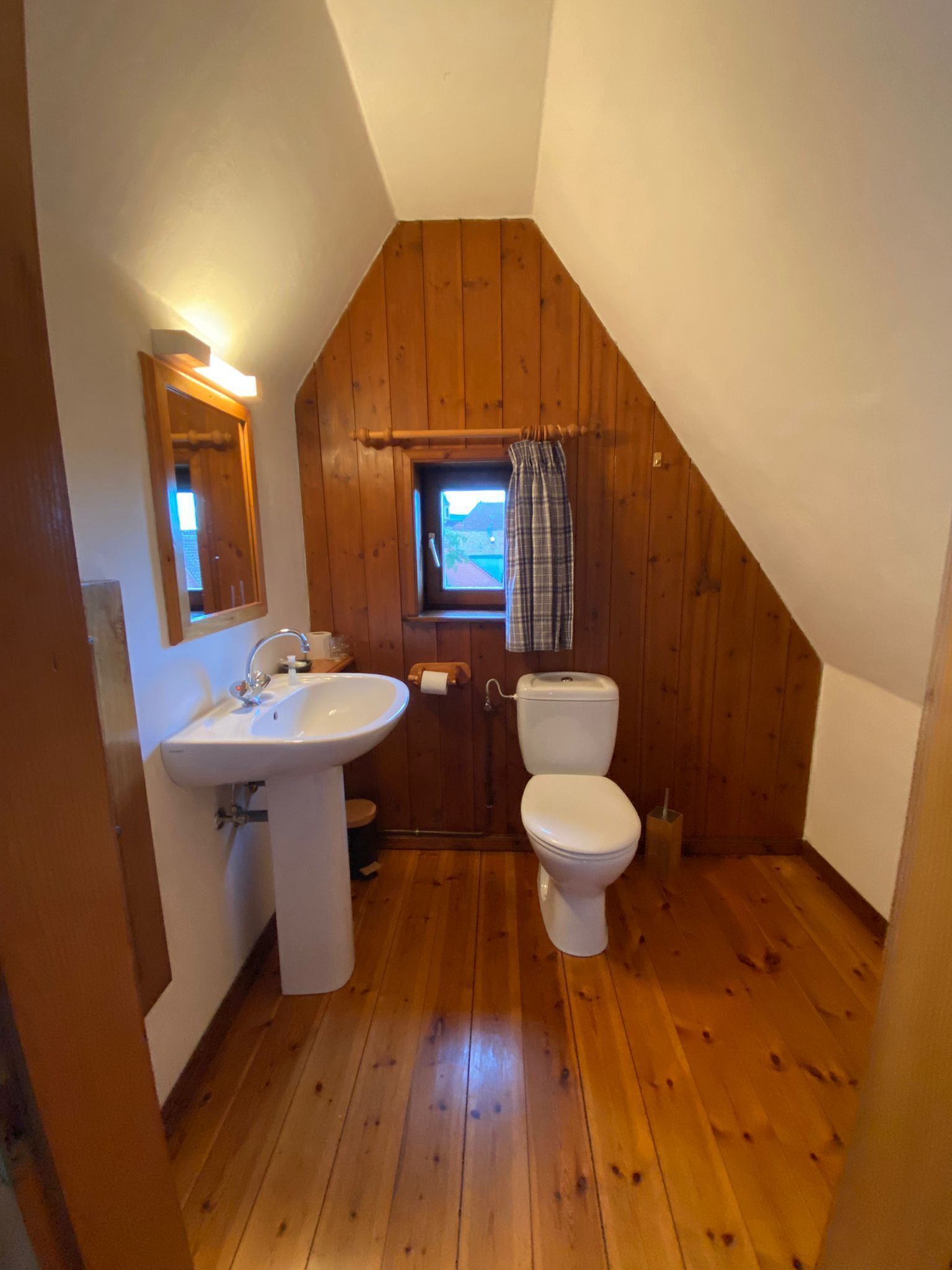 Ein kleines Badezimmer mit geneigtem Dach, Holzwänden, einem weißen Waschbecken und einer Toilette.