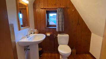 Ein kleines Badezimmer mit geneigtem Dach, Holzwänden, einem weißen Waschbecken und einer Toilette.
