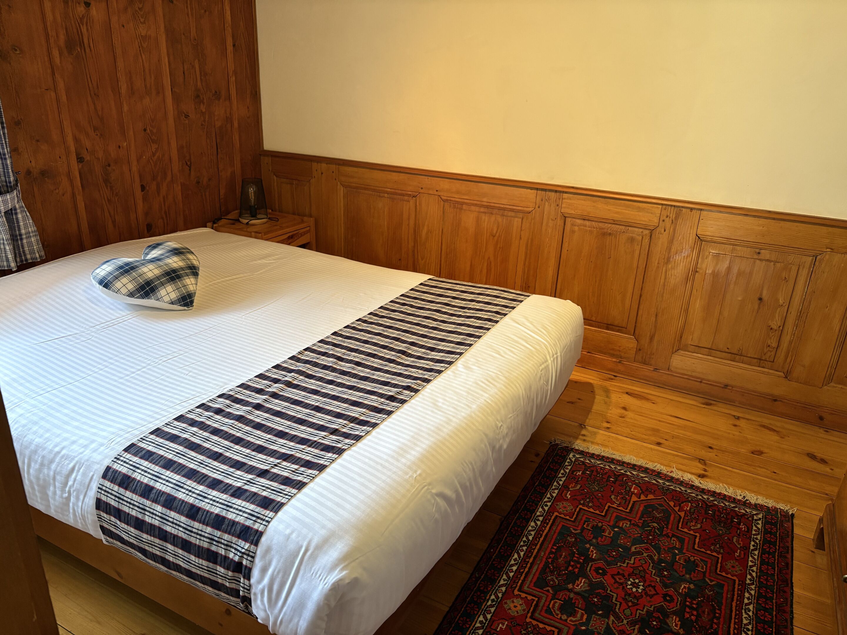 A bed with a heart-shaped pillow, a striped blanket, and a patterned rug.
