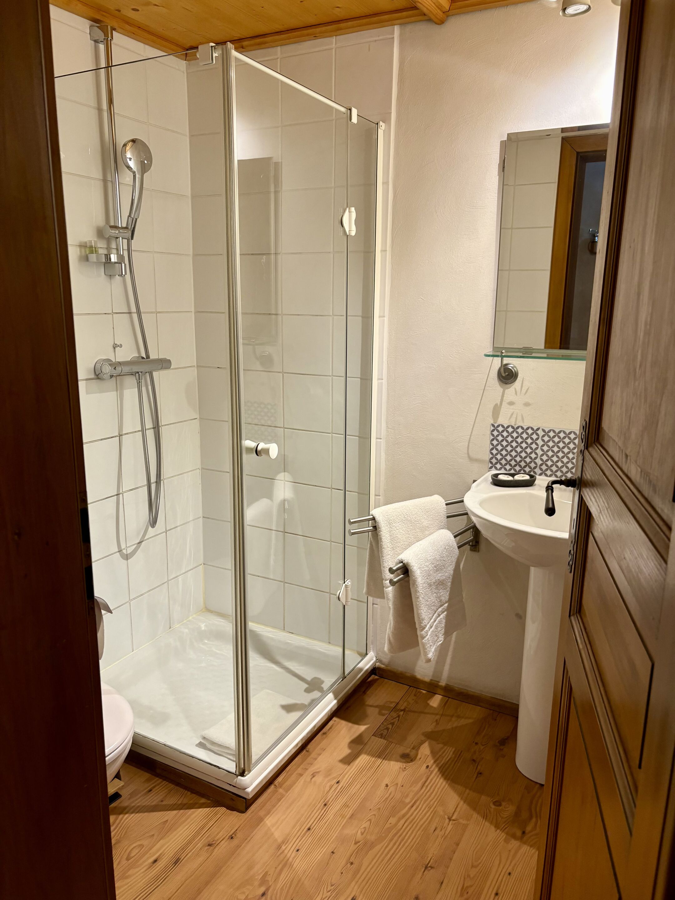 Une salle de bain avec une douche à parois de verre, un lavabo avec un miroir au-dessus et un revêtement de sol en bois.