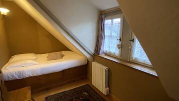 A small, sloped bedroom with a single bed, a radiator, a window with curtains, and a patterned rug.