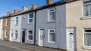 Una hilera de casas escalonadas con puertas y ventanas blancas, un cielo azul despejado y una calle visible.