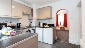 Cocina compacta con armarios blancos, un refrigerador pequeño y una encimera con diversos objetos.