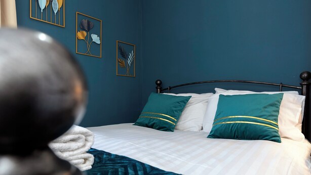Una cama con ropa de cama blanca y almohadas turquesa, un cabecero oscuro y una obra de arte en la pared.