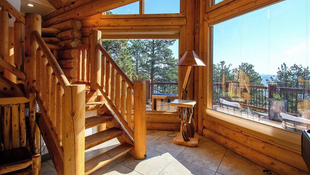 A wooden staircase leading to a balcony with a view of trees and a table with chairs. - Luxe Log Home+Views+Hot Tub+Fire Pit+Open Air Game Room + Red Rocks (Bailey)