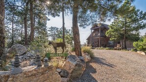 A rustic lodge with a welcoming sign, surrounded by a natural landscape with trees and a rock garden. - Luxe Log Home+Views+Hot Tub+Fire Pit+Open Air Game Room + Red Rocks (Bailey)