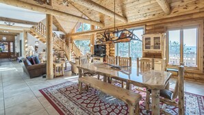 A spacious log cabin interior with a large dining table, wooden chairs, a staircase, and a chandelier. - Luxe Log Home+Views+Hot Tub+Fire Pit+Open Air Game Room + Red Rocks (Bailey)