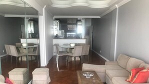 A spacious living room with a large beige sofa, a wooden coffee table, and a dining area with a glass table and chairs. - Stunning view! Sea Front! (Mucuripe Fortaleza)