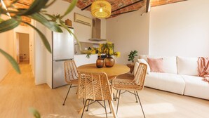 Una cocina moderna con techo de ladrillo, una zona de comedor con sillas de mimbre y un sofá blanco.