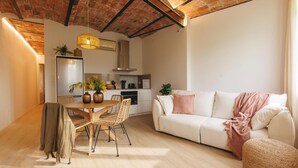 Una sala de estar moderna con un sofá blanco, un comedor con mesa y sillas de madera, y una cocina al fondo.
