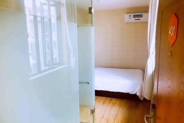 A hotel room with a bed, a window, and a door with a number sign.