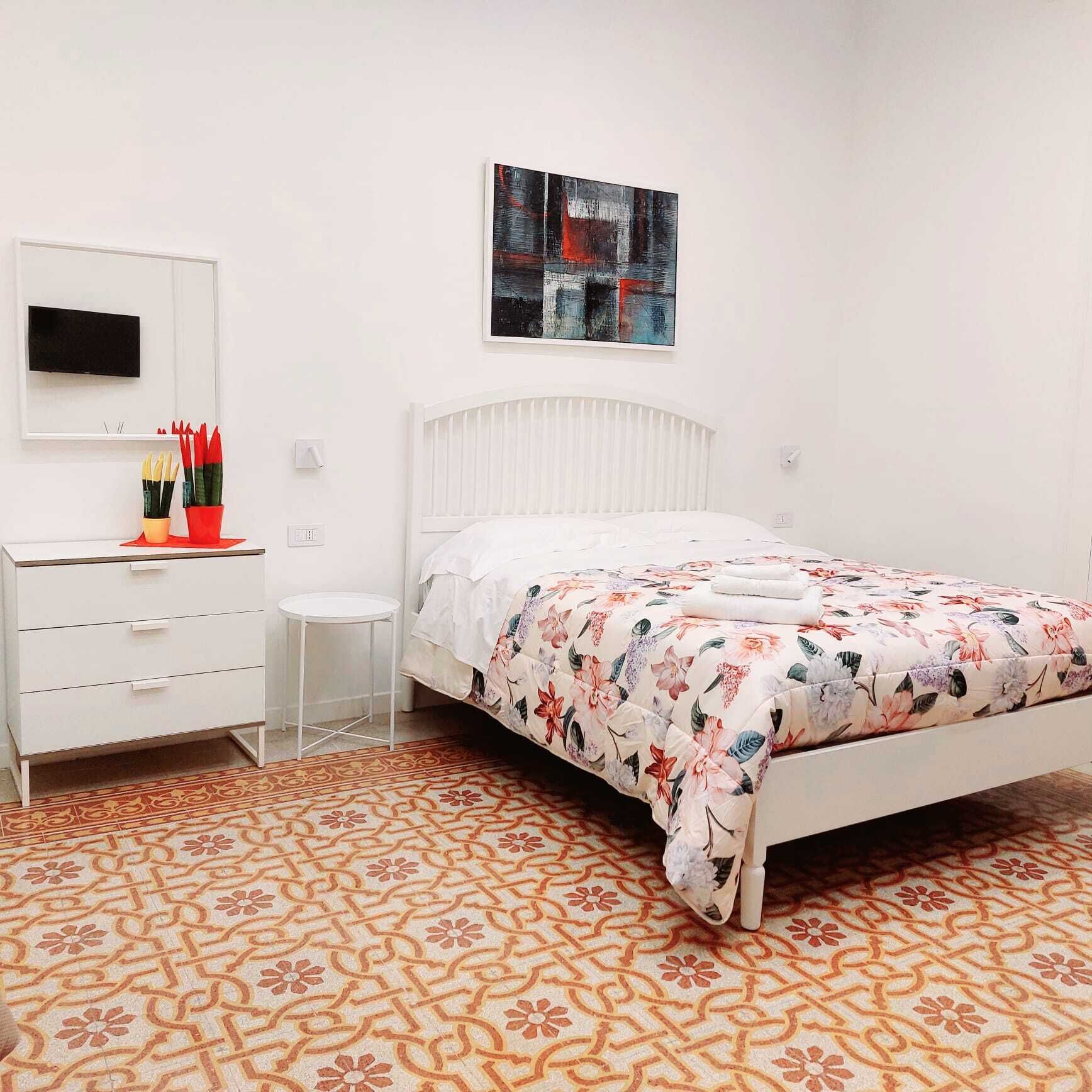 Un dormitorio con una cama, un escritorio con una silla, una mesita pequeña y un televisor montado en la pared.