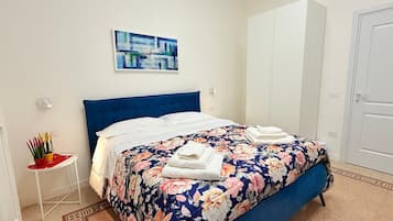 Un dormitorio con una cama, una colcha estampada, un cabecero azul, un cuadro en la pared y un armario blanco.